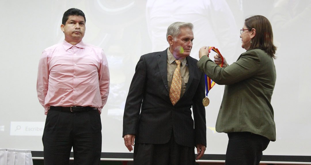 La Rectora junto al Secretario General realiza imposición de medalla al doctor Espinosa.